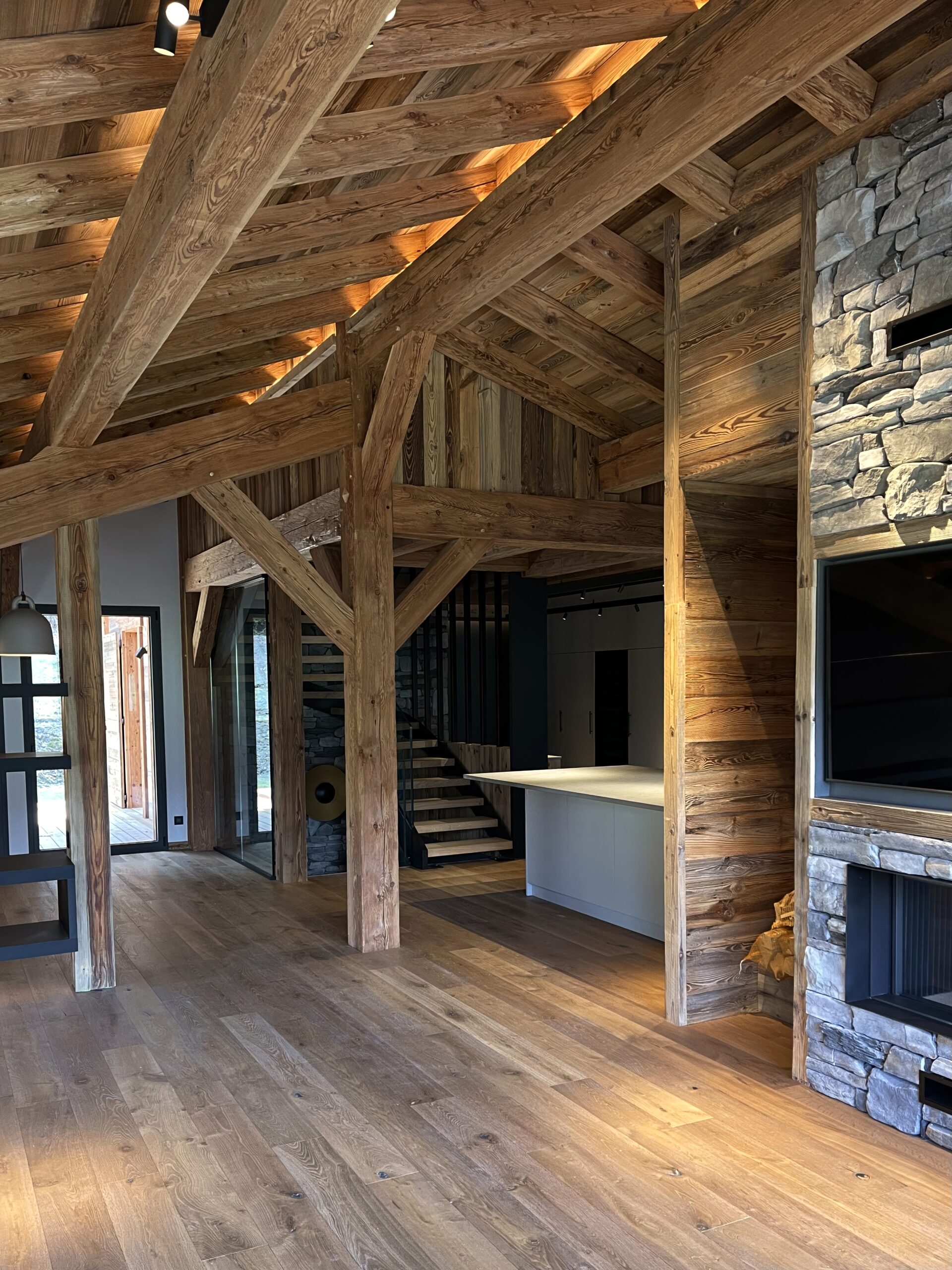 Architecture d'intérieur chalet luxe Alpes avec charpente en bois apparente et cheminée en pierres