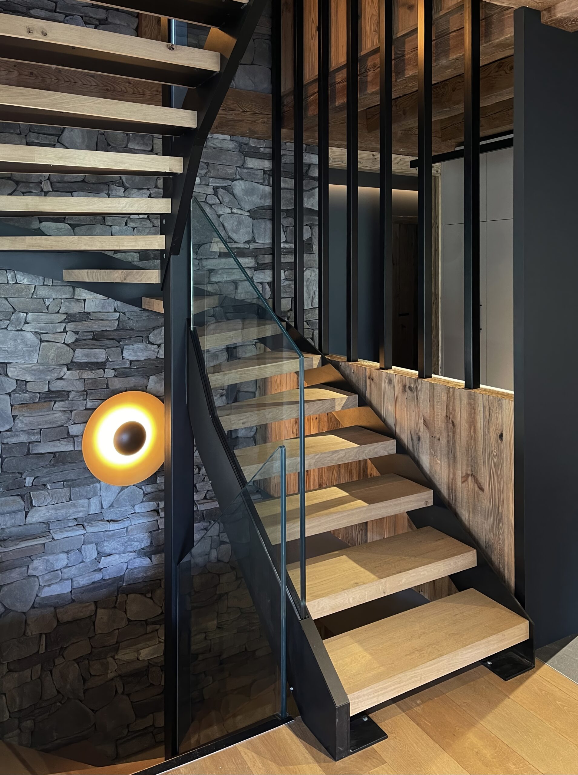 Architecte d'intérieur chalet luxe à Megève avec escalier sur mesure en bois et en métal et murs en pierres