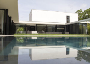 Extension moderne villa d'architecte Lyon avec grandes baies vitrées en aluminium noir, brises-soleil et piscine miroir