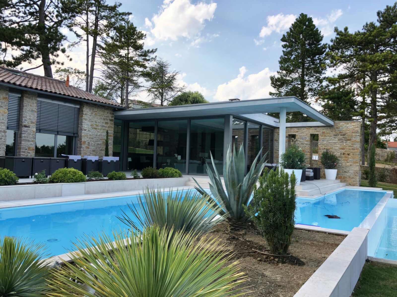 Extension moderne maison d'exception en pierres dans les Monts d'Or avec auvent porte-à-faux et piscine à débordement