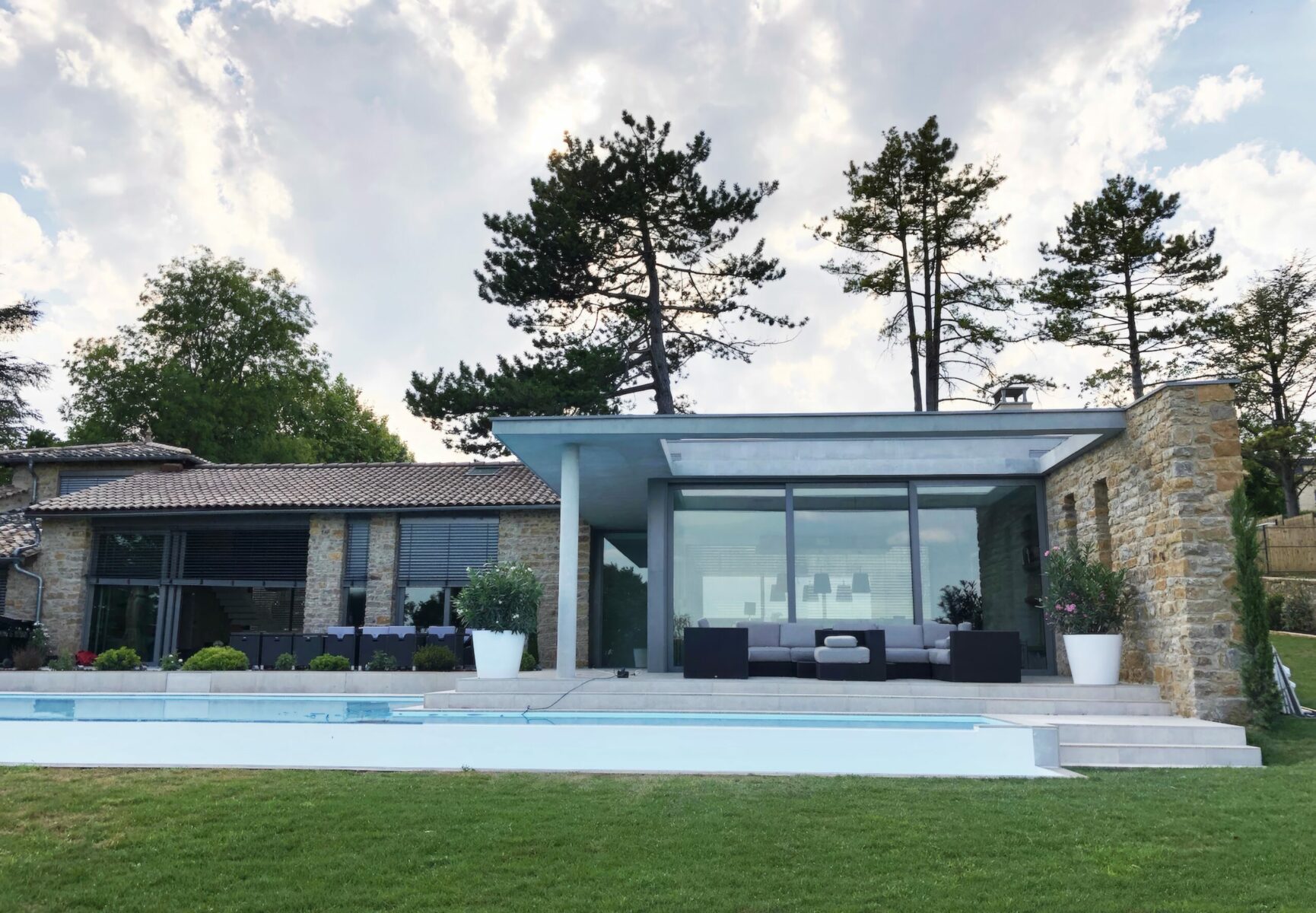 Architecte spécialisé extension moderne maison existante pierres Lyon avec piscine à débordement et grandes ouvertures en aluminium